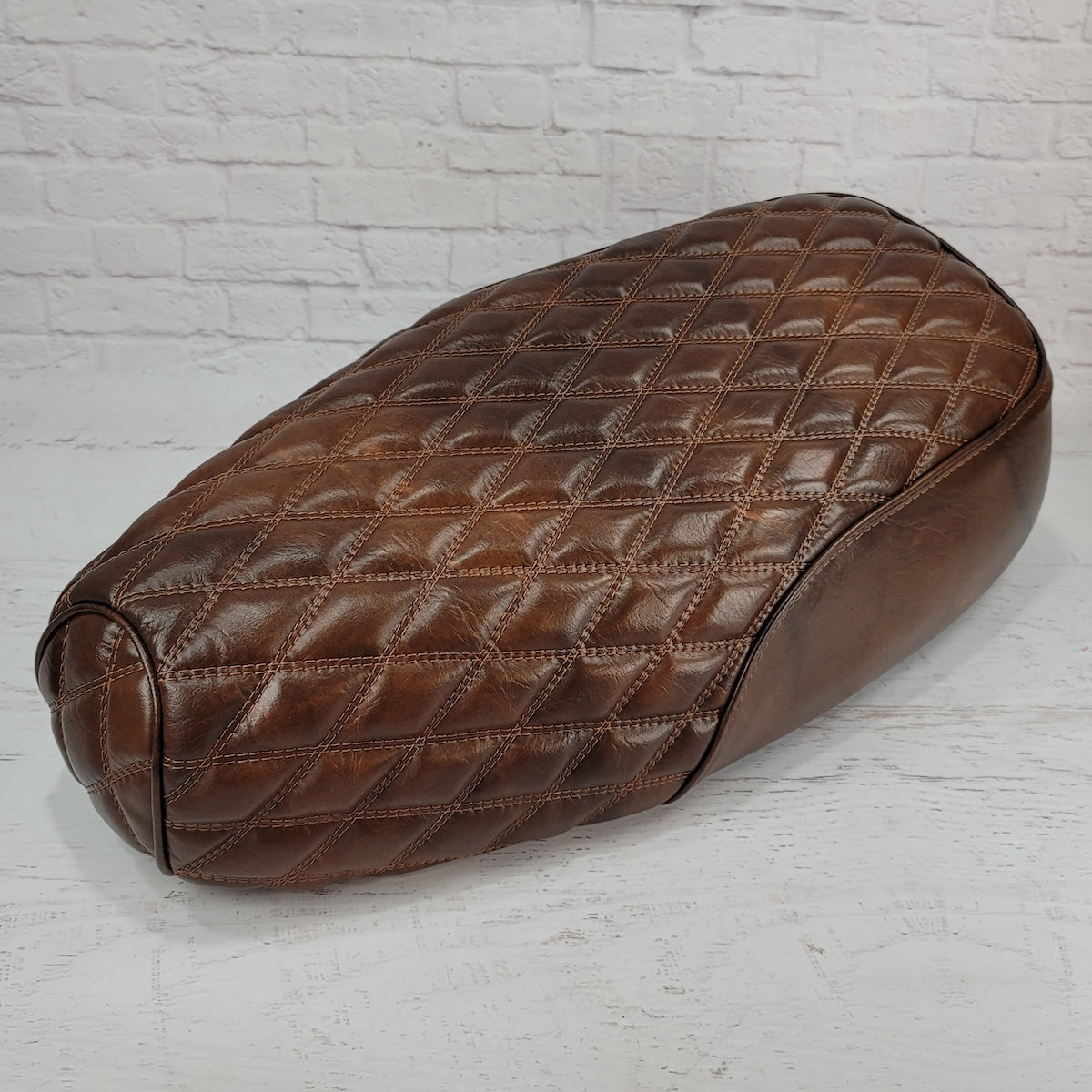 Lower front angle of a distressed tobacco brown Genuine Buddy Kick 125 seat cover with matching diamond stitching and piping, handmade by Cheeky Seats