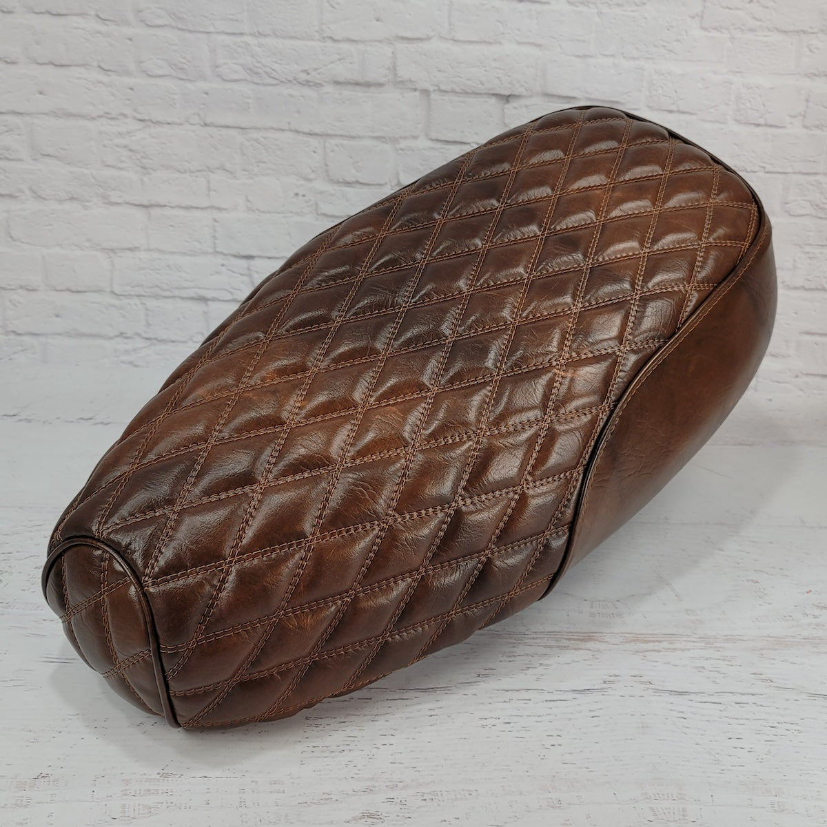 Front three-quarter view of a distressed tobacco brown Genuine Buddy Kick 125 seat cover with diamond stitching and piping, handmade by Cheeky Seats