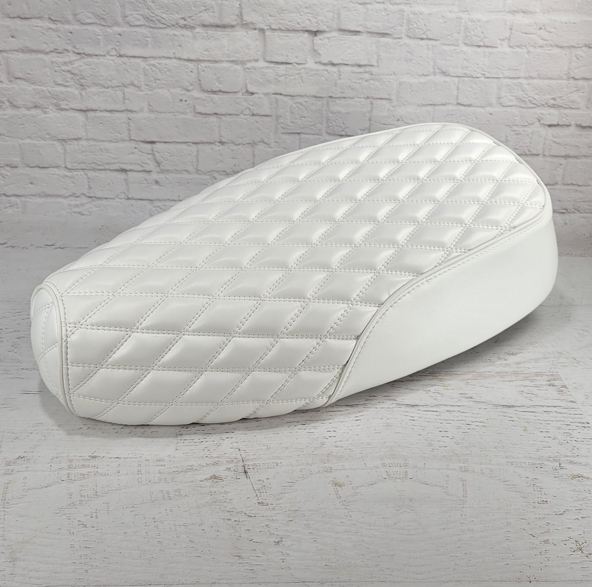 Lower front three-quarter view of a white Genuine Buddy Kick 125 seat cover with matching diamond stitching and piping, handmade by Cheeky Seats