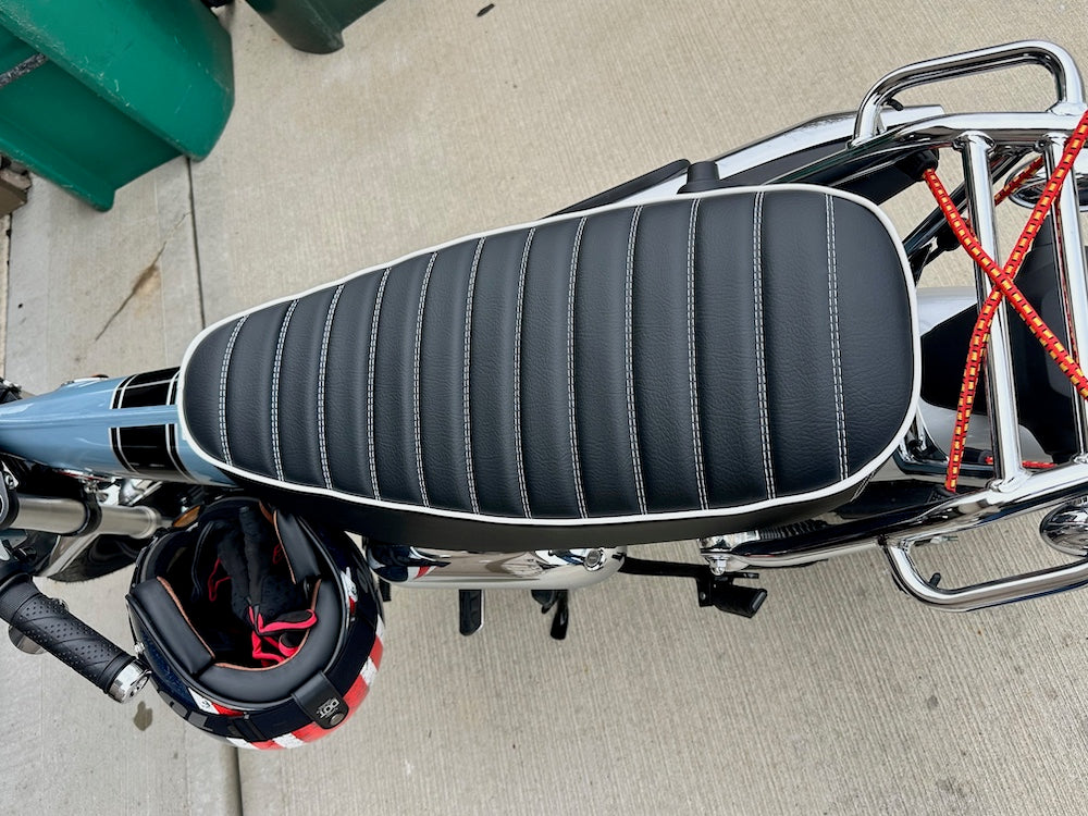 Overhead view of a black tuck-and-roll Honda DAX 125 seat with white stitching, piping, chrome rack and helmet, handmade by Cheeky Seats