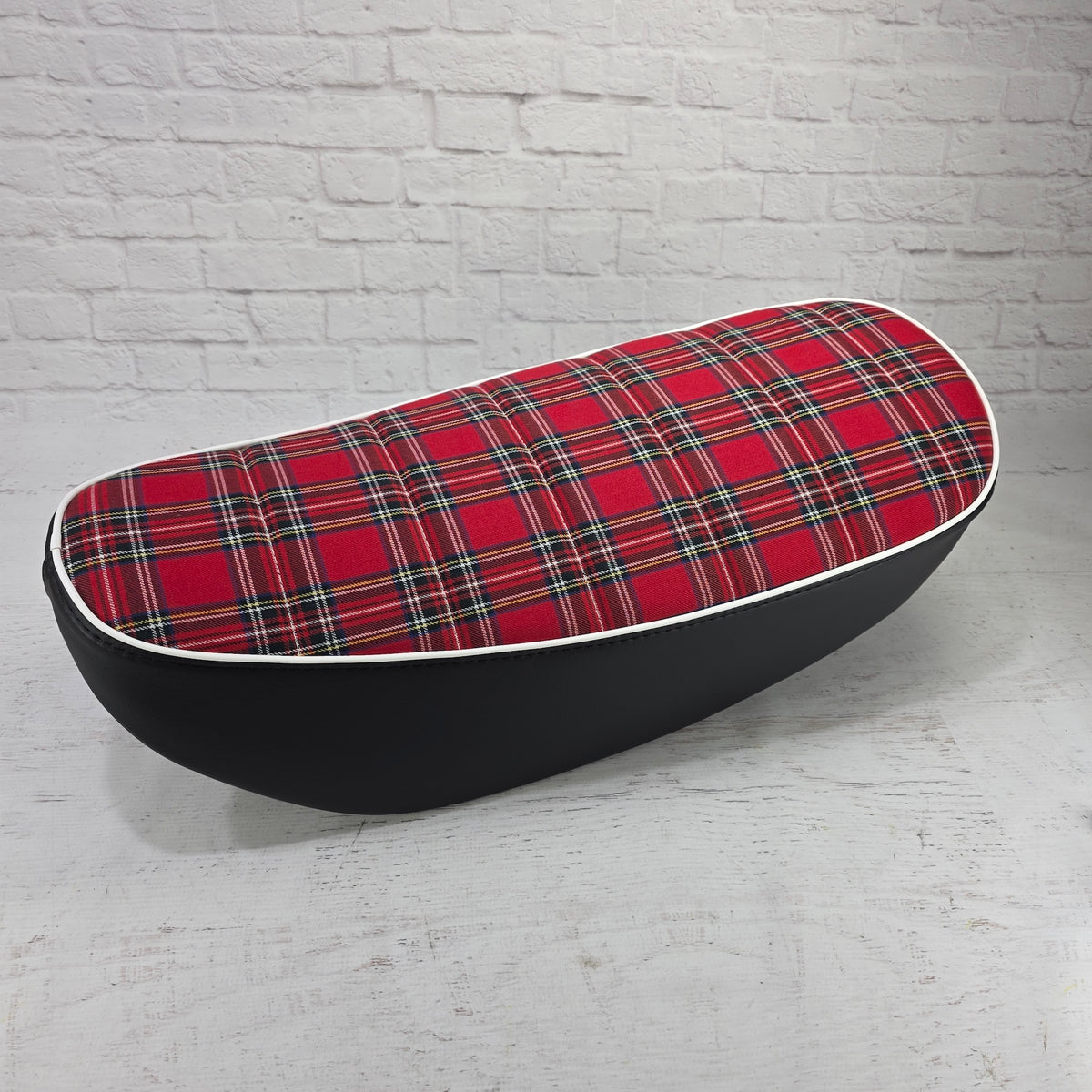 Side view of a red tartan plaid tuck-and-roll Honda DAX 125 seat cover with white piping, handmade by Cheeky Seats