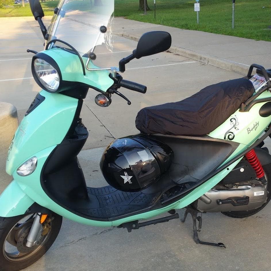 Mint Genuine Buddy fitted with a black Cheeky Seats rain cover, with helmet on the floorboard