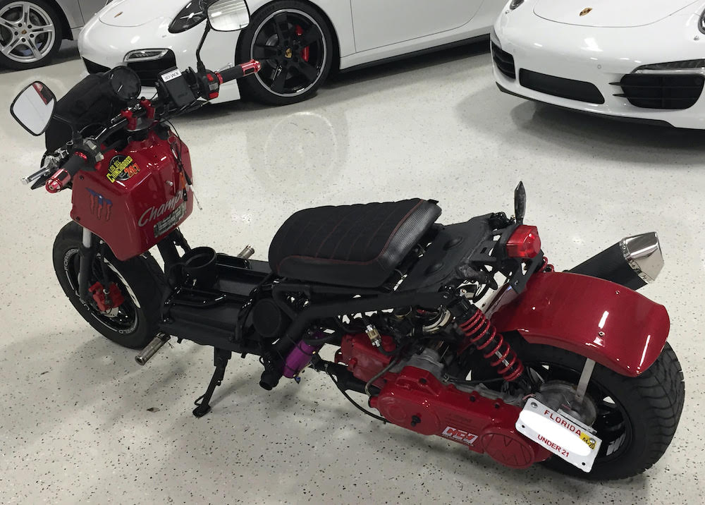 Customer photo of a red Maddog scooter in a garage with the black Bride fabric seat cover installed, overhead view, handmade by Cheeky Seats