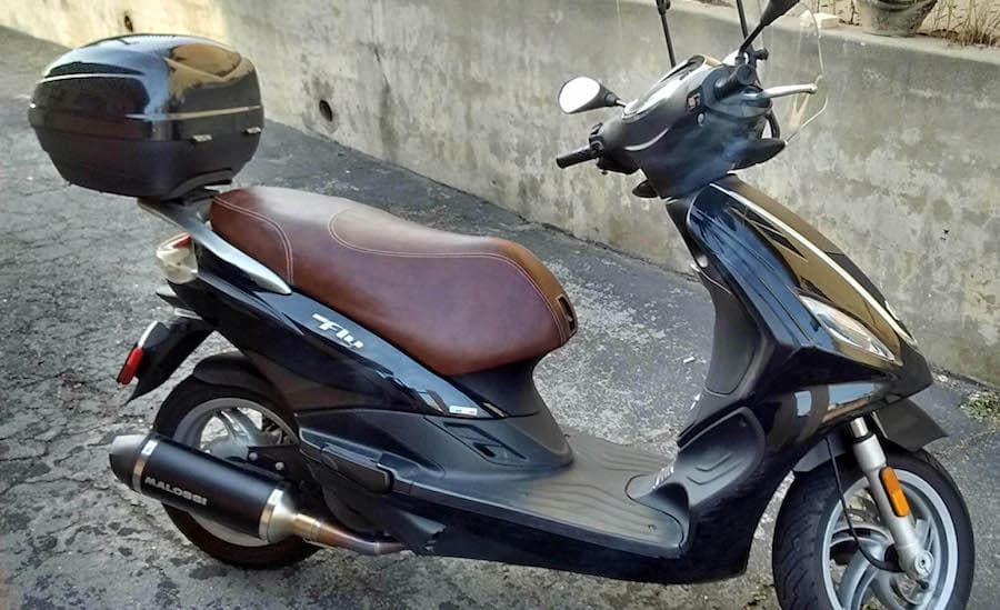 Black Piaggio Fly scooter with a whiskey brown French-seam seat cover and rear top case, handmade by Cheeky Seats