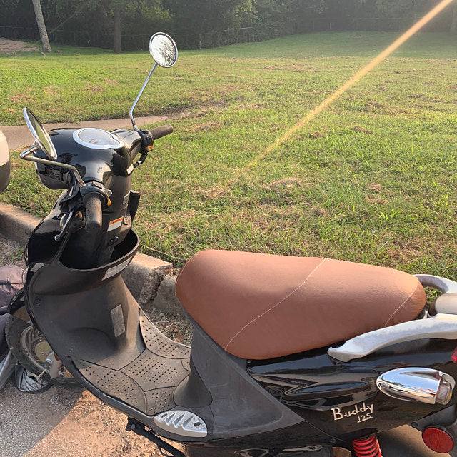 Cinnamon-brown Cheeky Seats cover installed on a black Genuine Buddy 125, left-side view