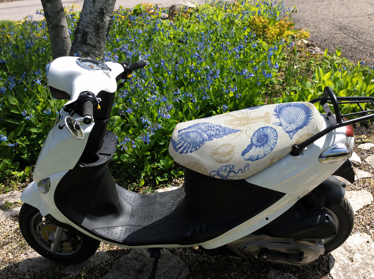 Beachcomber coastal seat cover fitted to a white Genuine Buddy scooter in a flower garden, handmade by Cheeky Seats.