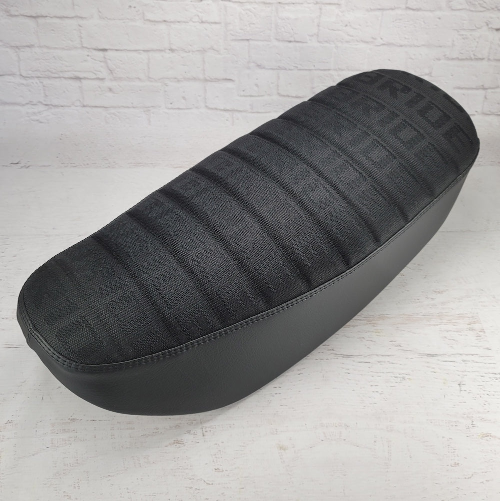 Angled view of a black BRIDE Honda DAX 125 tuck-and-roll cover with subtle woven lettering, handmade by Cheeky Seats