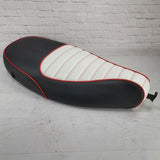 A two-tone padded seat cover for a Vespa ET, featuring black and white with red cross stitching and red piping handmade by Cheeky Seats