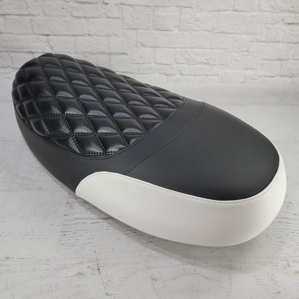 Front three-quarter view of a black Yamaha Zuma II BWS 49/50 Prebug seat cover with a padded diamond panel and white side accent, handmade by Cheeky Seats