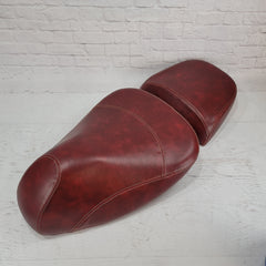 Vespa GTV split saddle seat cover in distressed oxblood with french seams on a white brick background