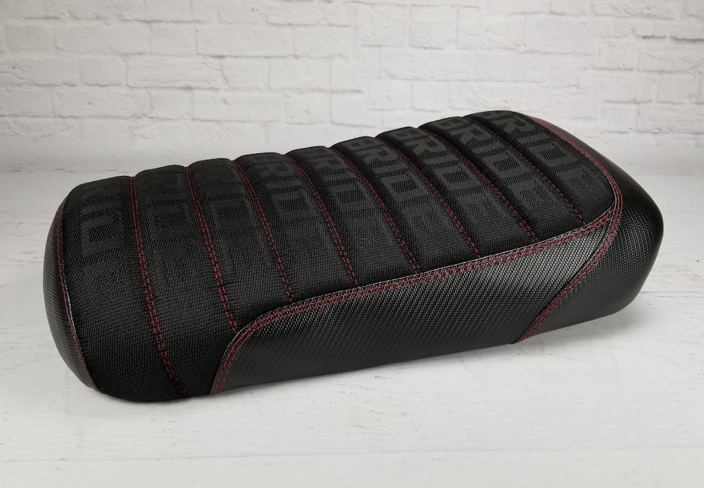 Rear three-quarter view showing padded Bride fabric pleats with red stitching and carbon-fiber-look black side panels, handmade by Cheeky Seats